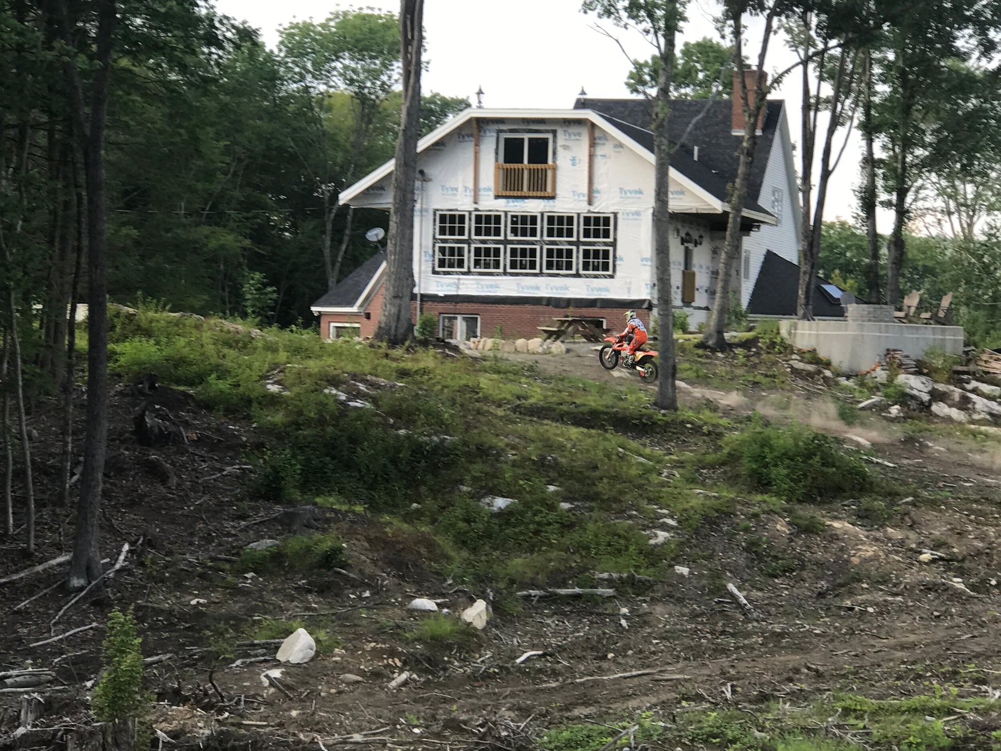 House under construction with a person riding on a KTM 350  in a wooded area.