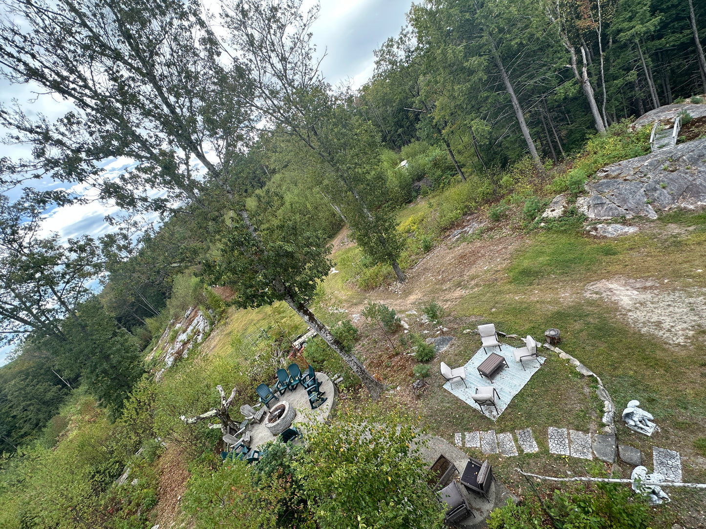 Outdoor setting with chairs, a table, and a blanket on a grassy hillside with trees.