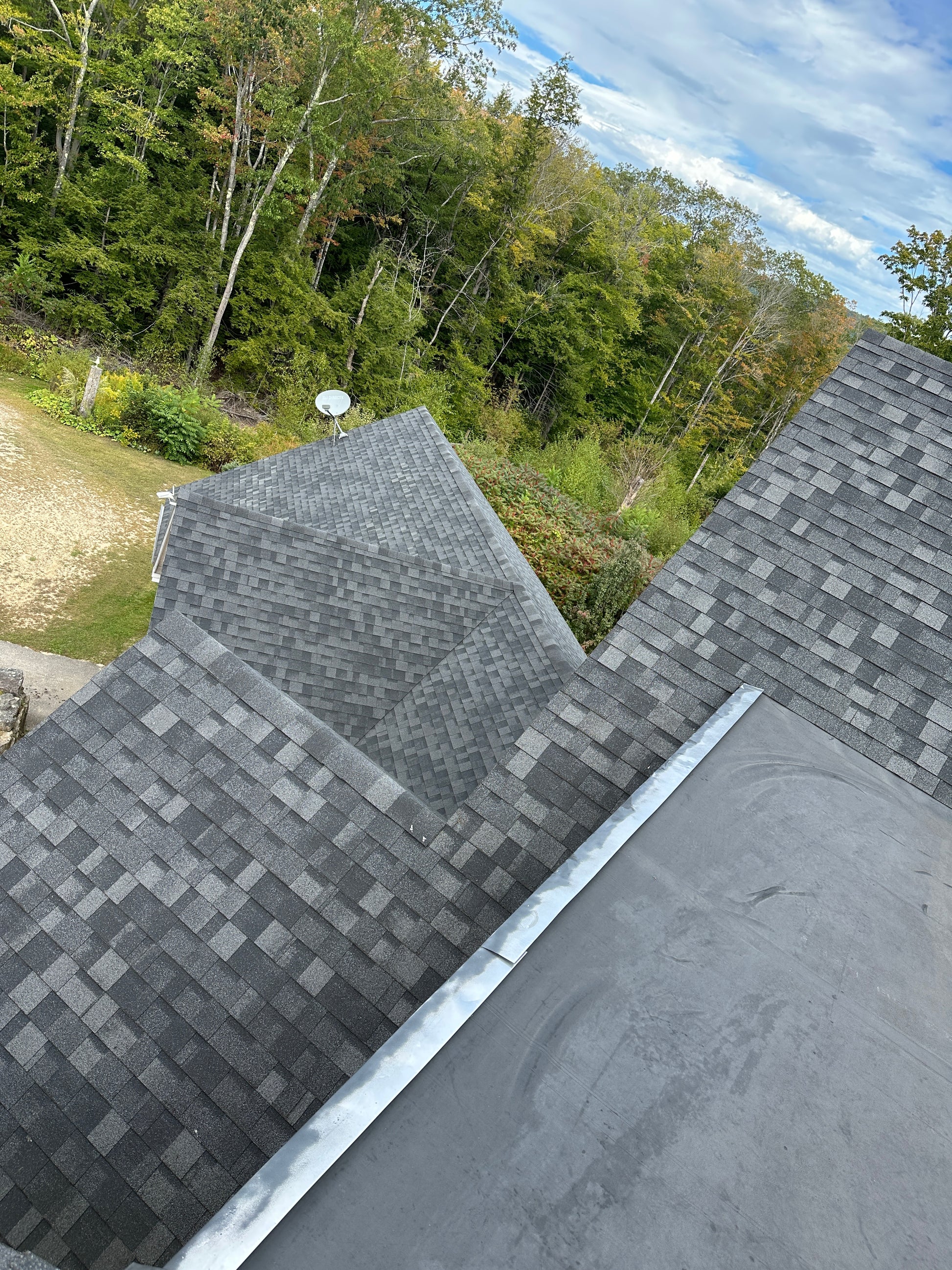 Roof with gray shingles and a view of trees and sky.