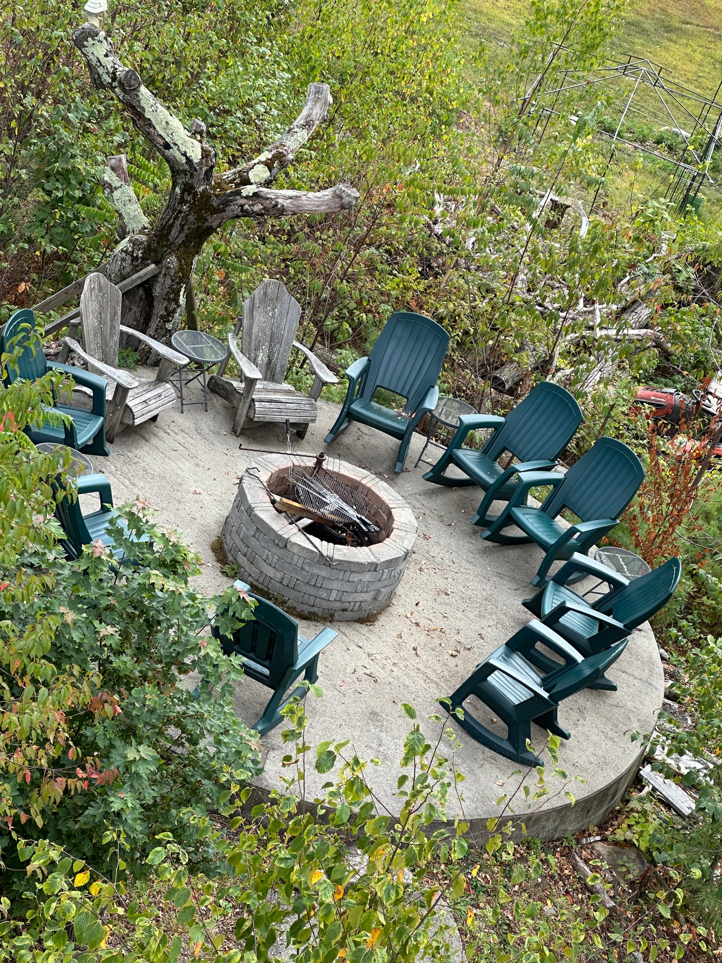 Outdoor setting with green chairs around a fire pit, surrounded by trees and grass.