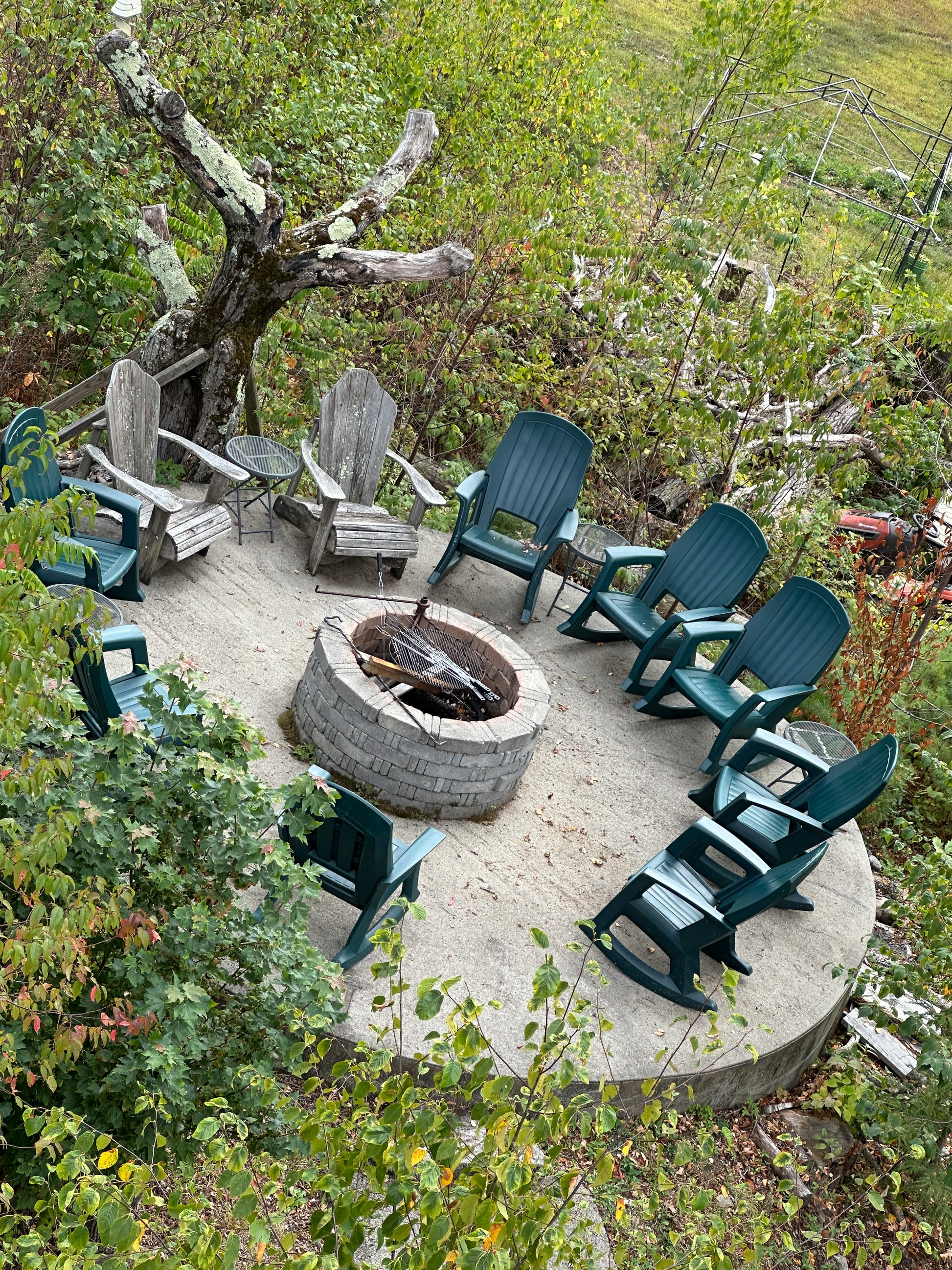Outdoor setting with green chairs around a fire pit, surrounded by trees and grass.