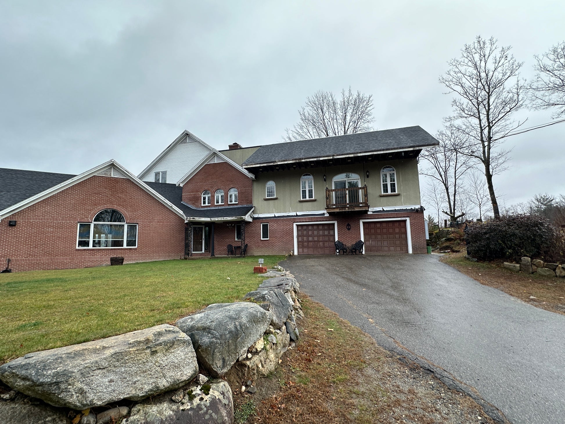 House with a brick facade and a stone wall in front on a cloudy day. Green lawns.
