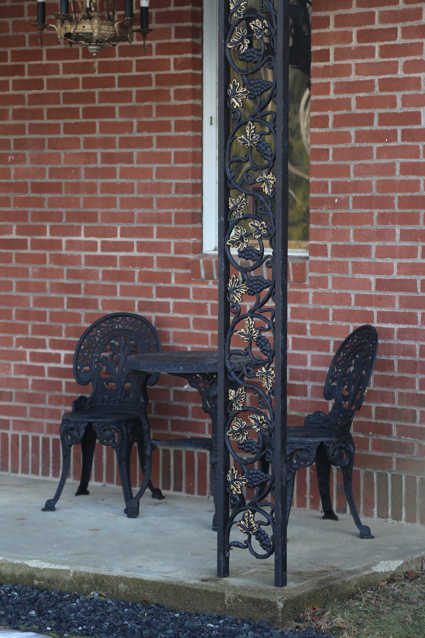 Black wrought iron garden set  outdoor furniture set against a brick wall. with wrought iron posts with gold leafing