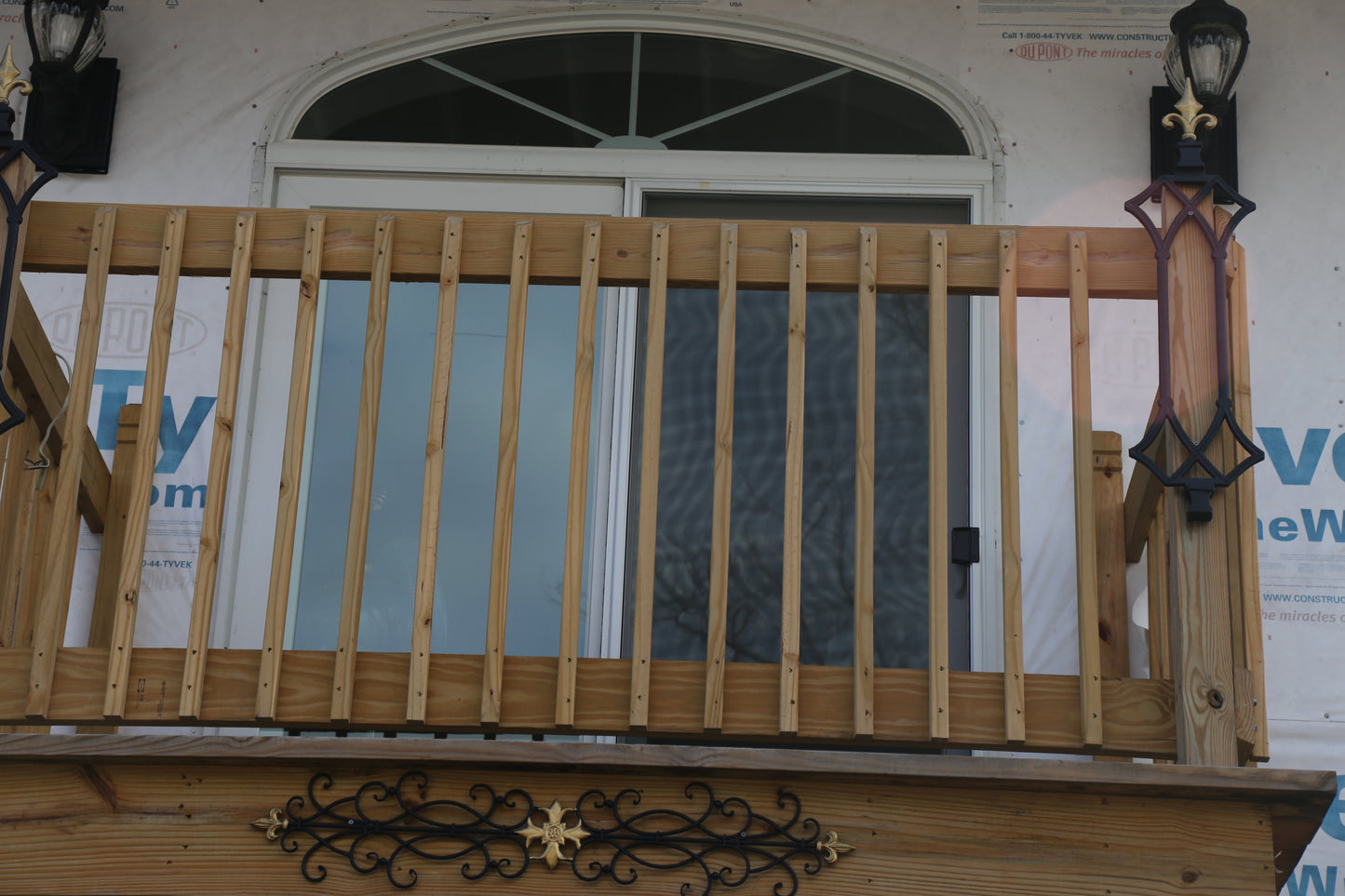 Wooden railing with decorative elements on a porch, with construction materials in the background.