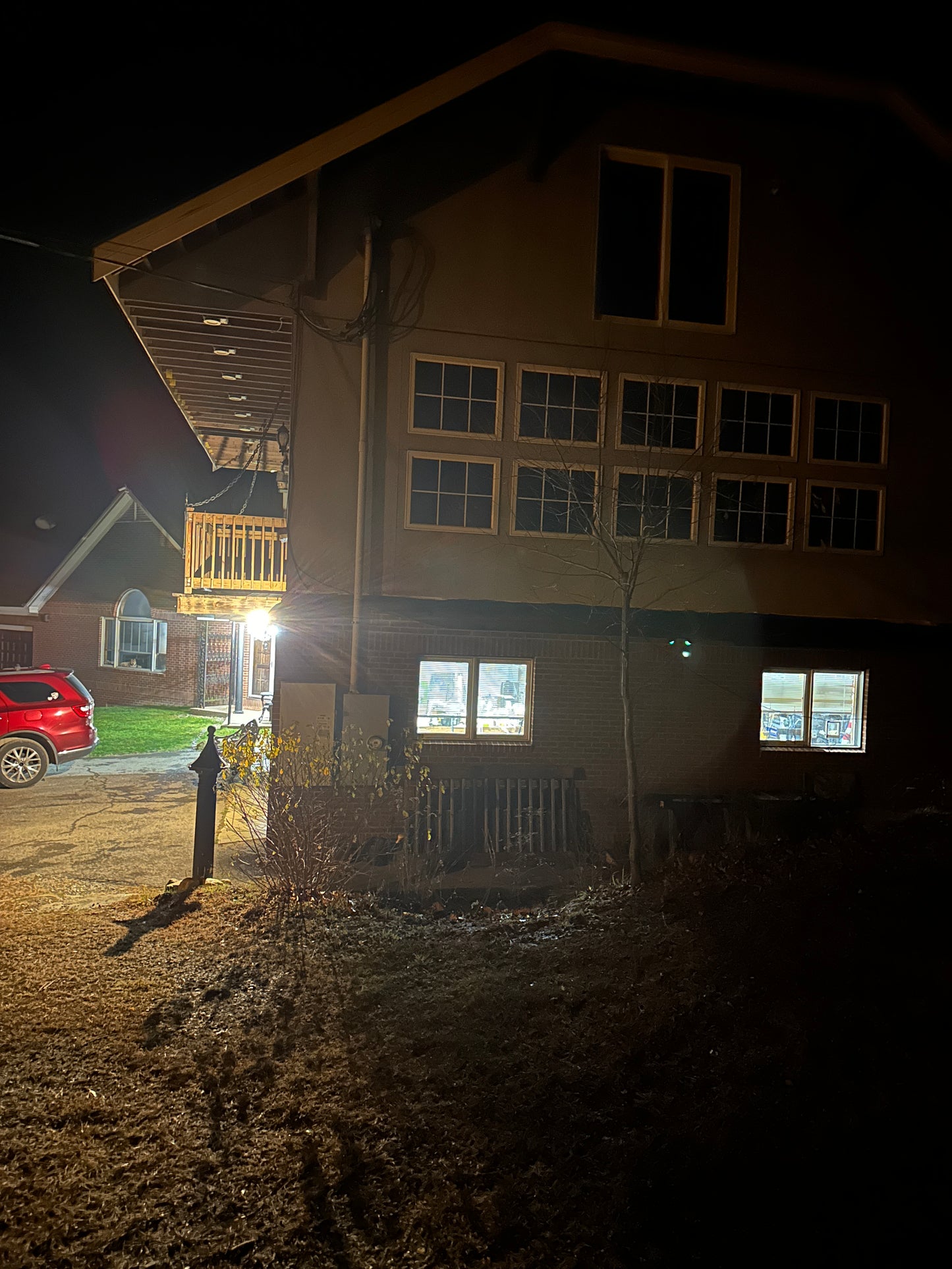 At night with a building and a red car parked on the side. Garage lights on