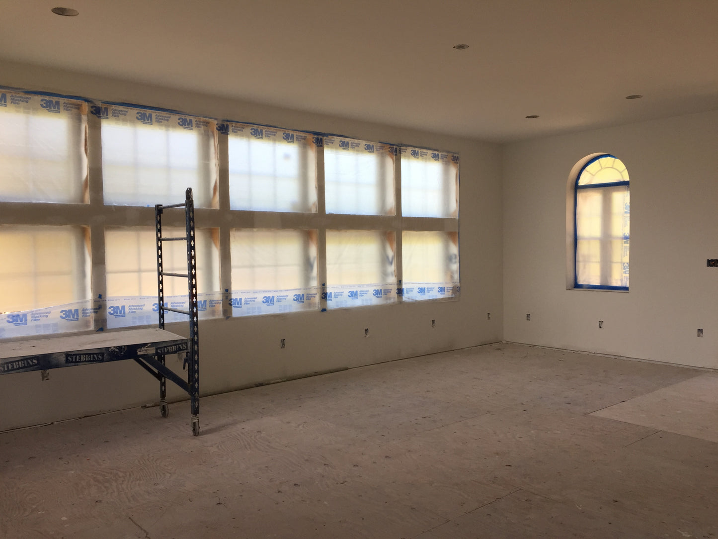 Room under construction with large windows and a ladder.