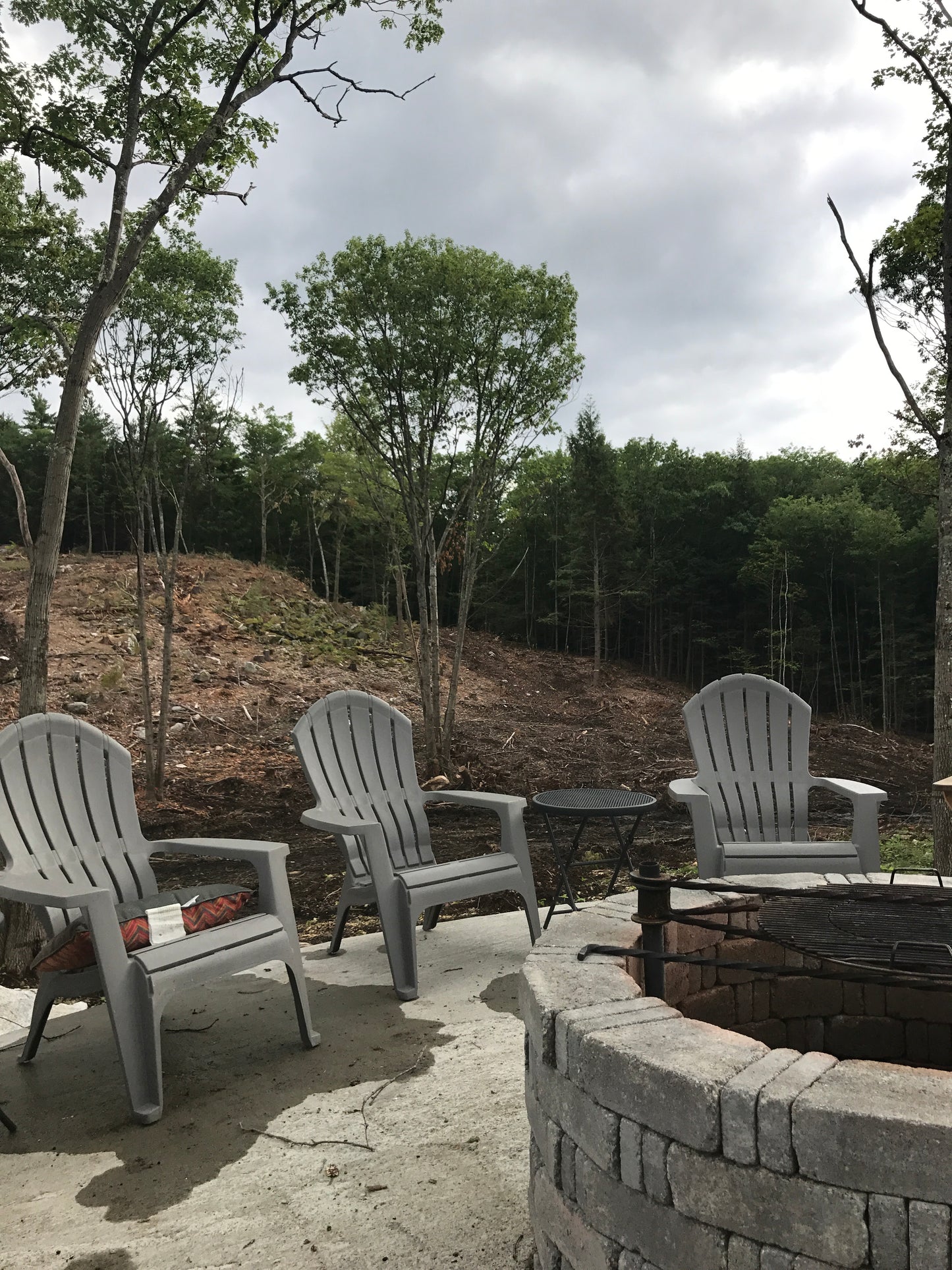 Outdoor patio area with white chairs and a fire pit surrounded by trees.