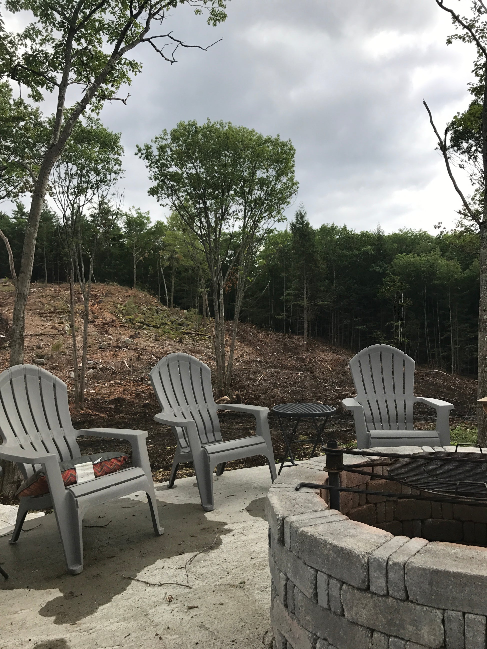 Outdoor patio area with white chairs and a fire pit surrounded by trees.