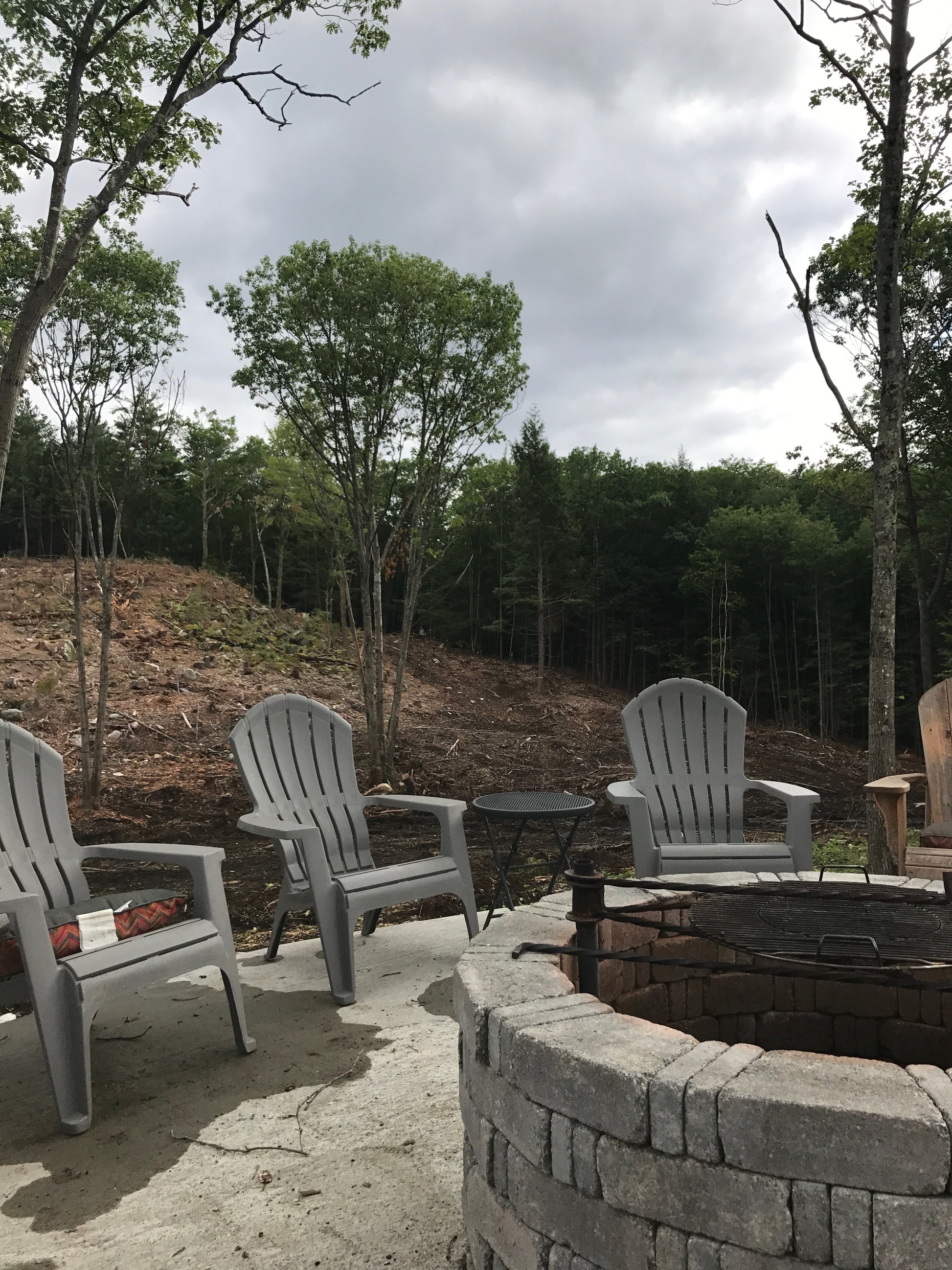Outdoor patio with gray chairs and a fire pit area surrounded by trees.