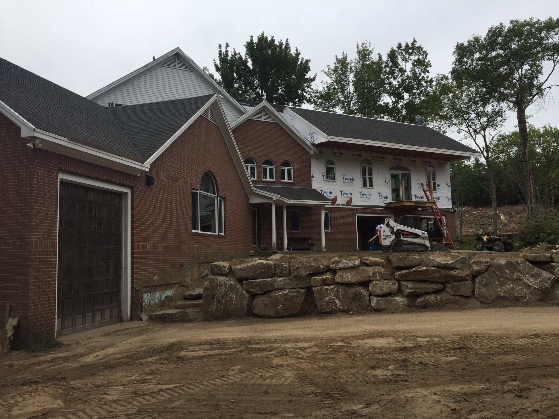 Brick house with a stone retaining wall in front, construction materials visible