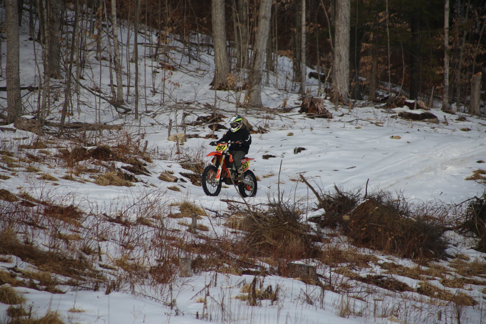 Person riding a KTM 350 dirt bike on a snowy trail in a forest Nature View NH Estate.