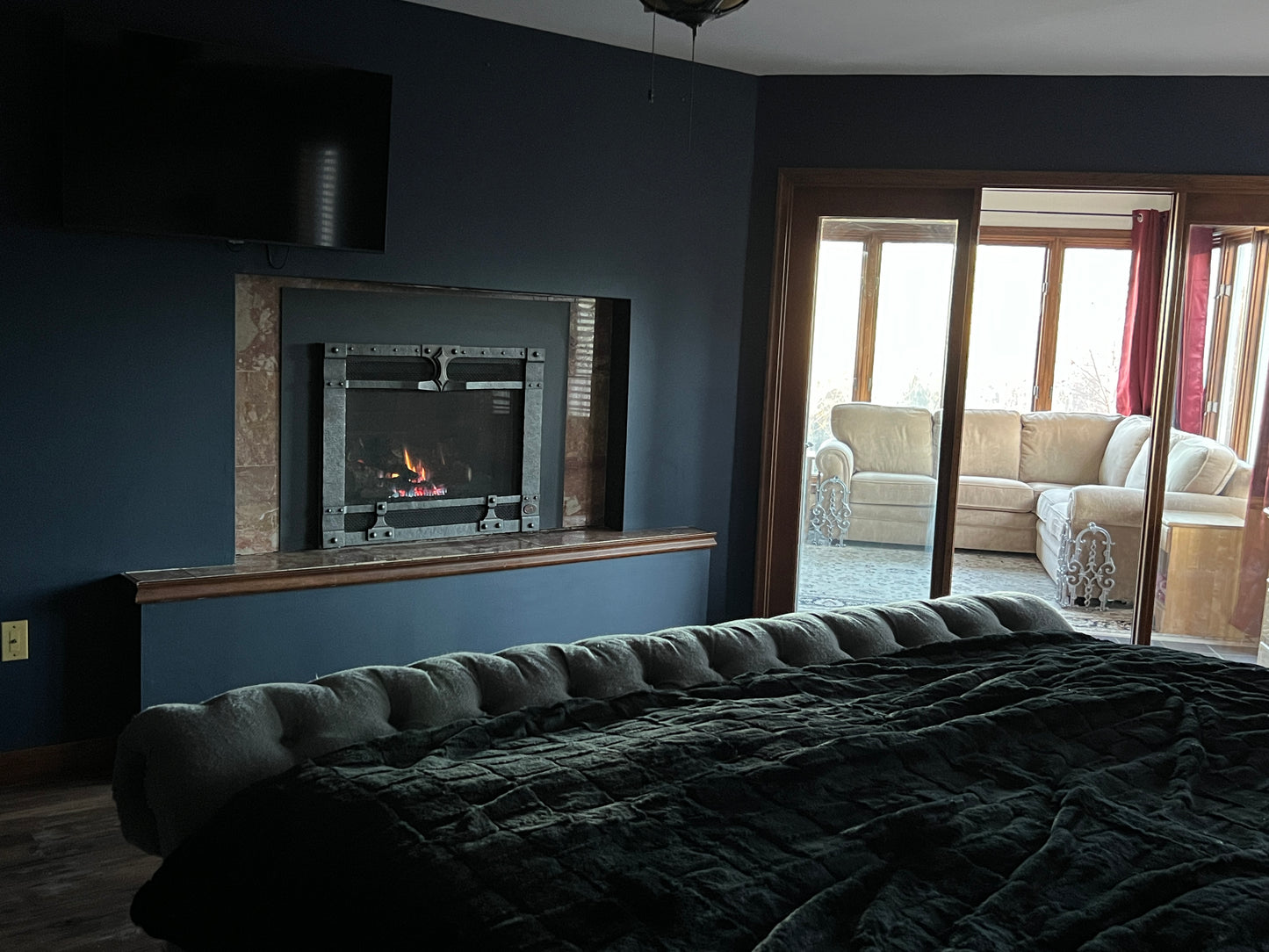 Room with a bed, fireplace, and view of a living room through a glass door.