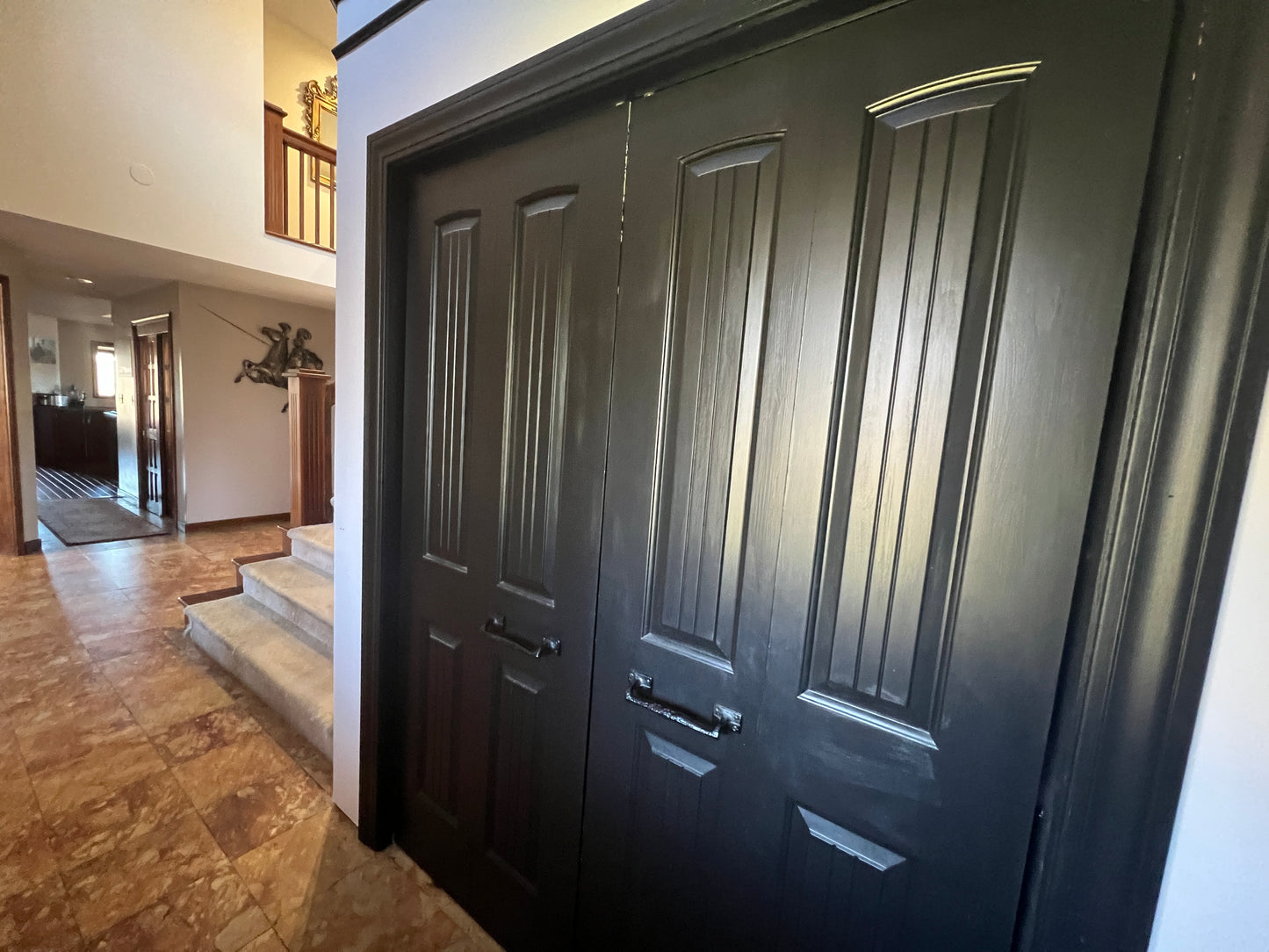 Dark wooden door of a house with a hallway and staircase in the background.