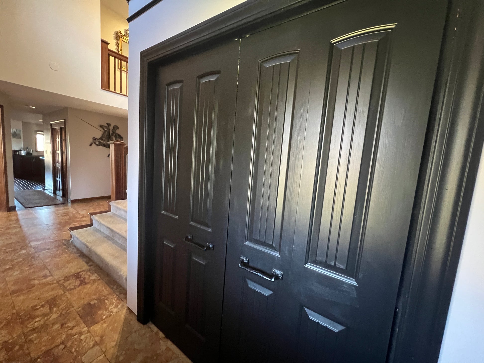 Dark wooden door of a house with a hallway and staircase in the background.