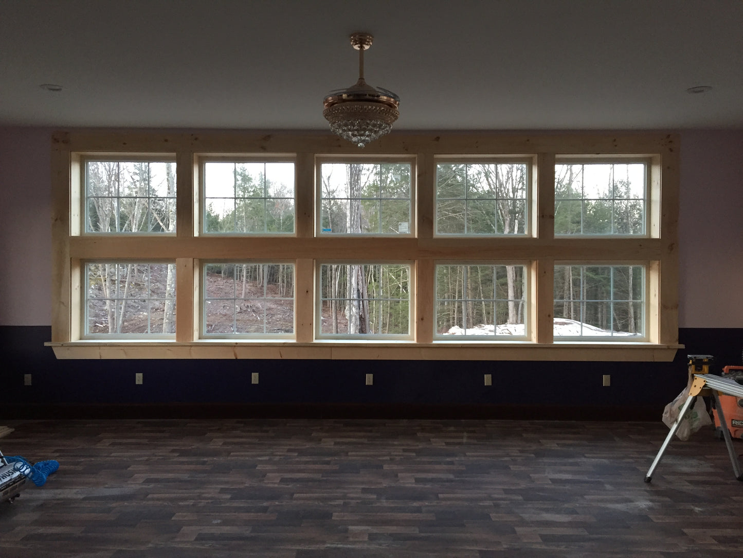 Room with large windows showing trees, wooden beams, and a chandelier.