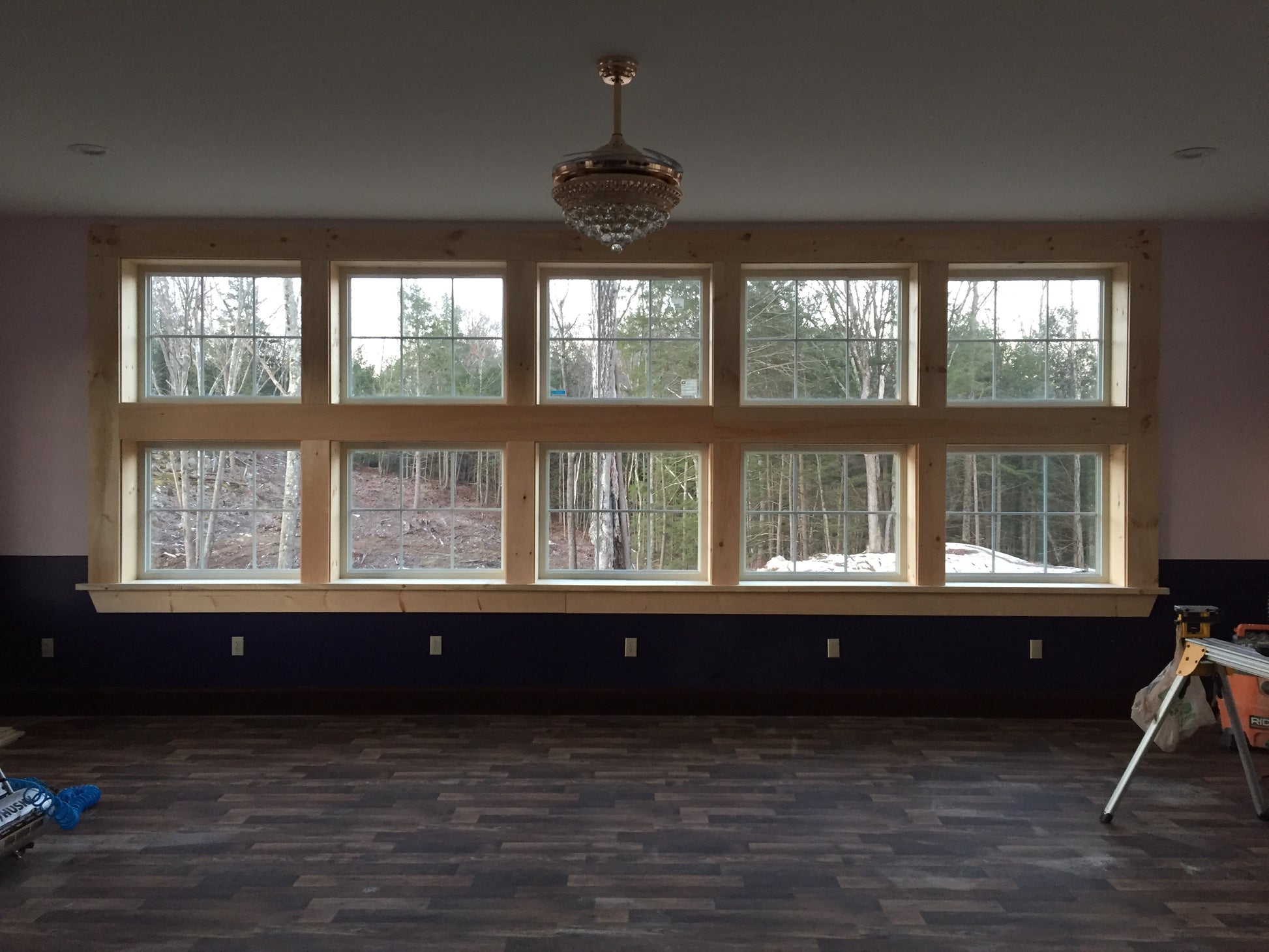Room with large windows showing trees, wooden beams, and a chandelier.