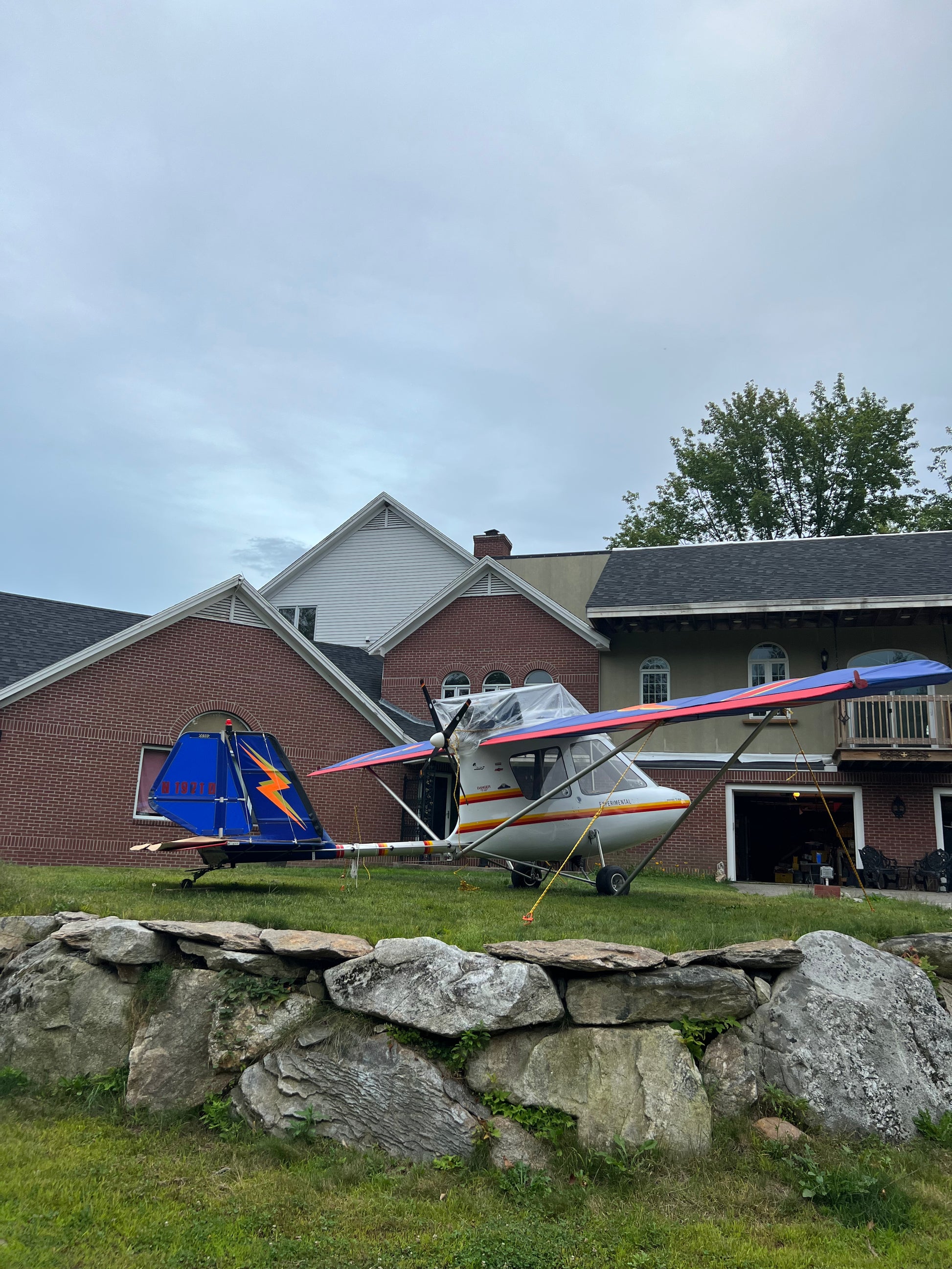 Small airplane on a grassy area with a stone wall and buildings in the background.