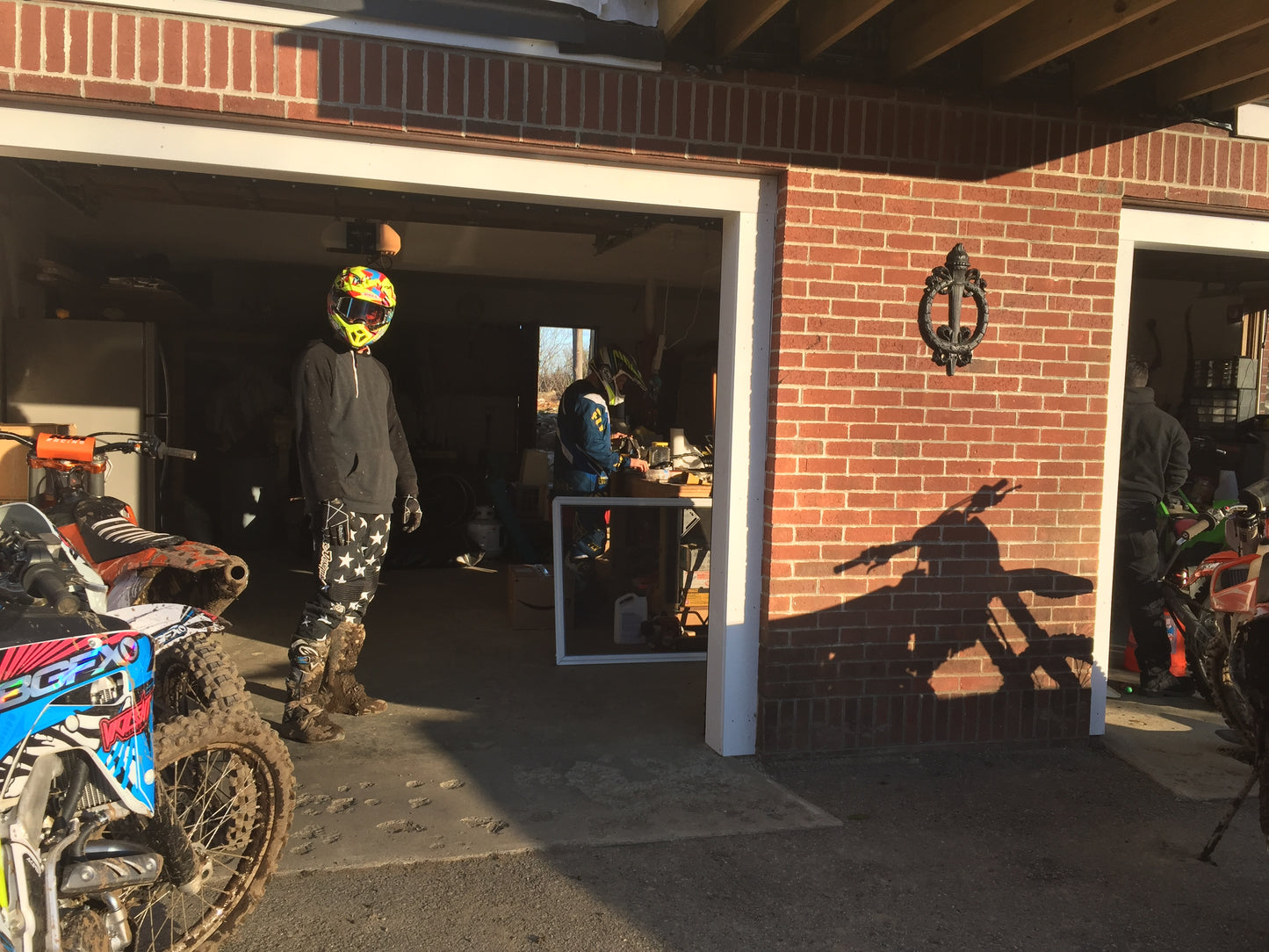Person wearing a helmet standing in front of a garage with motorcycles and a table inside.