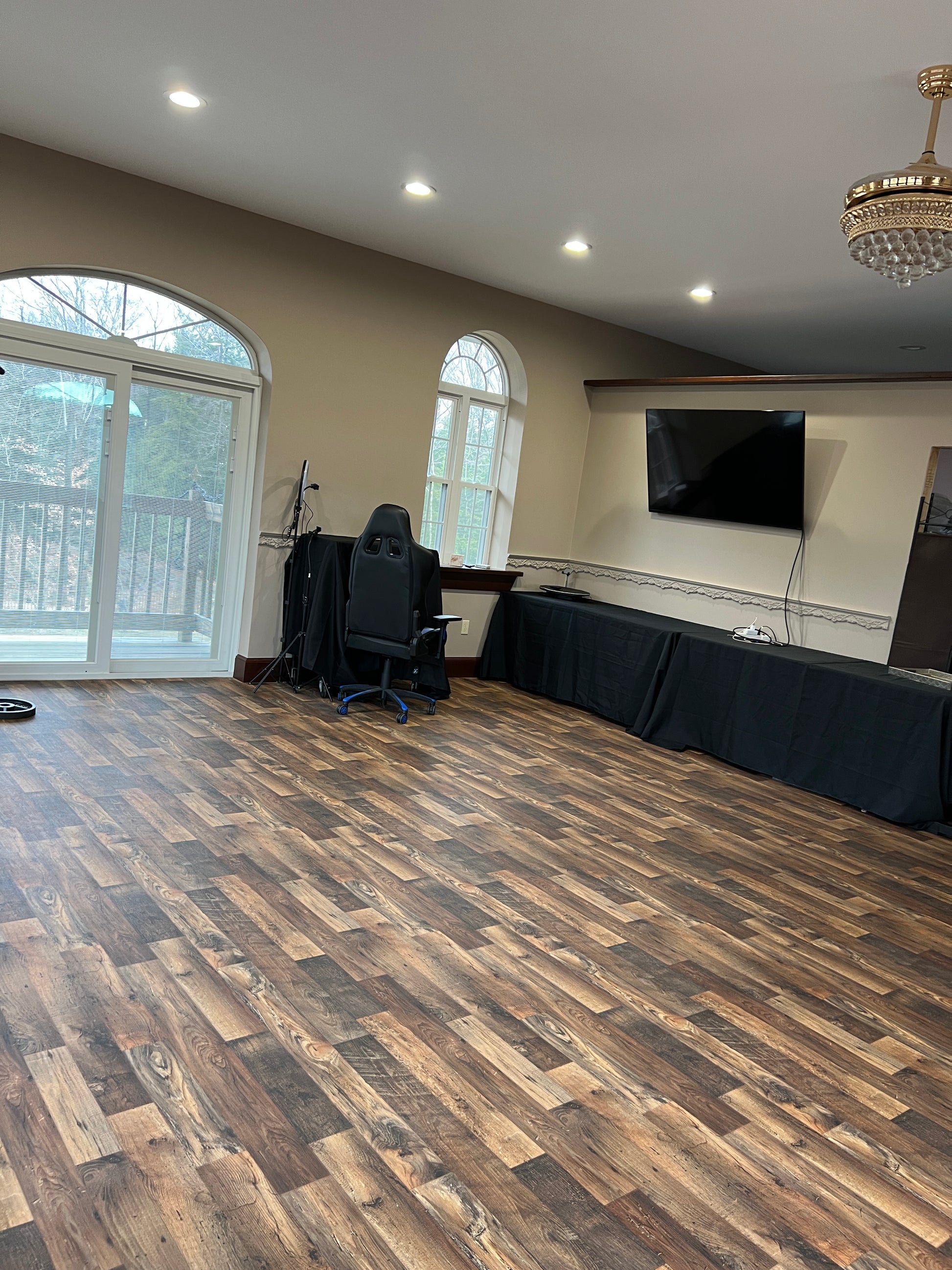 Room with wooden flooring, large arched  windows, and a chandelier.