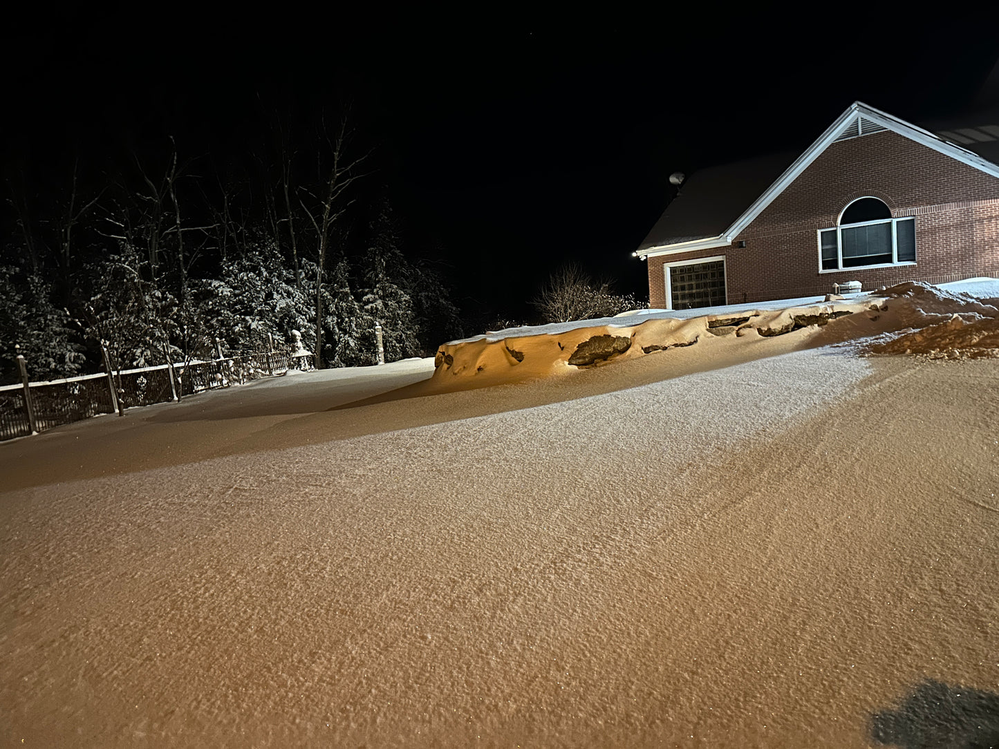 Snow-covered landscape in front of a house at night. Wrought iron fencing lines the snow.
