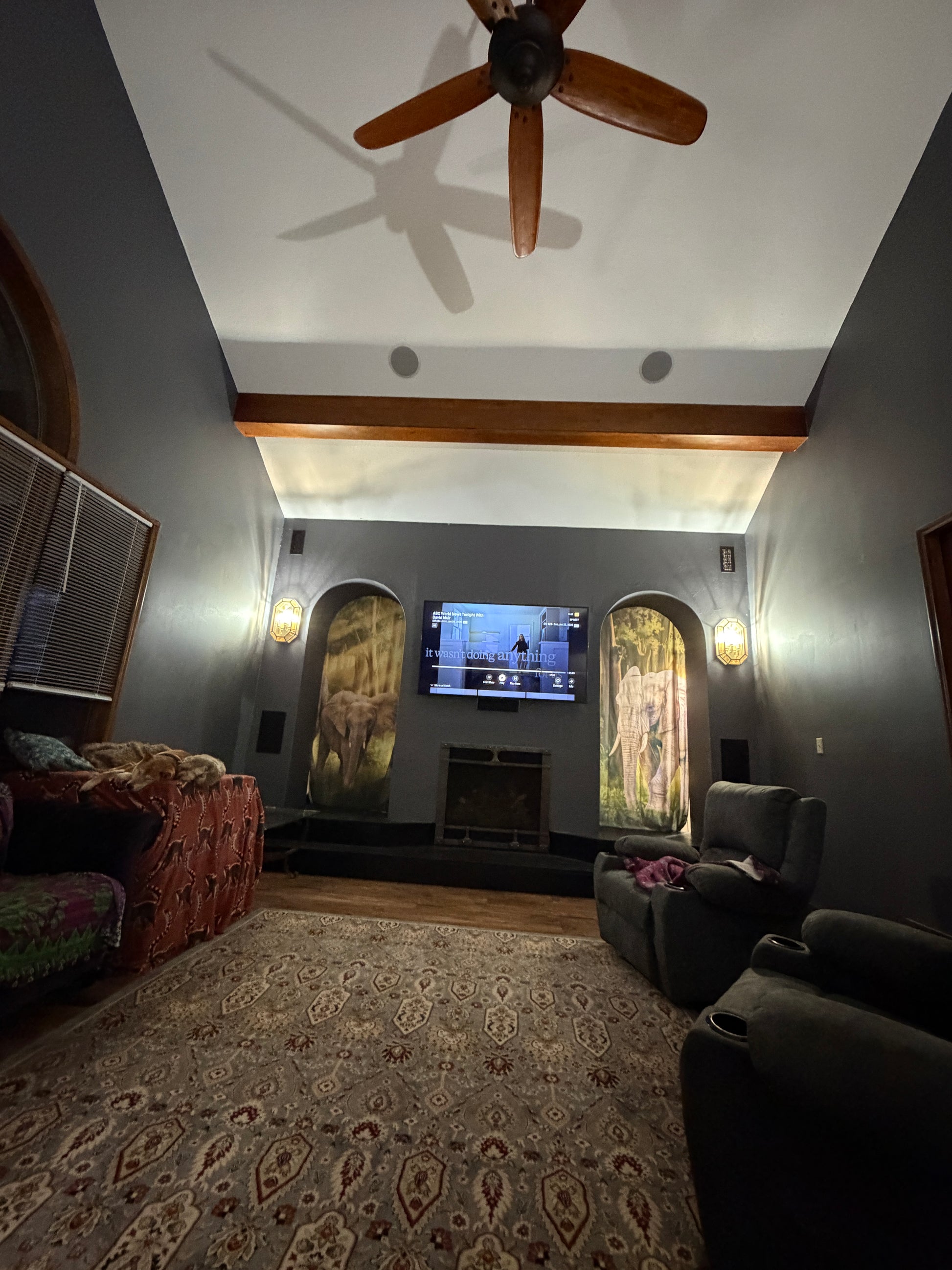 Living room with a ceiling fan, TV, and patterned rug. Arched doorways with an illuminated elephant on fabric.
