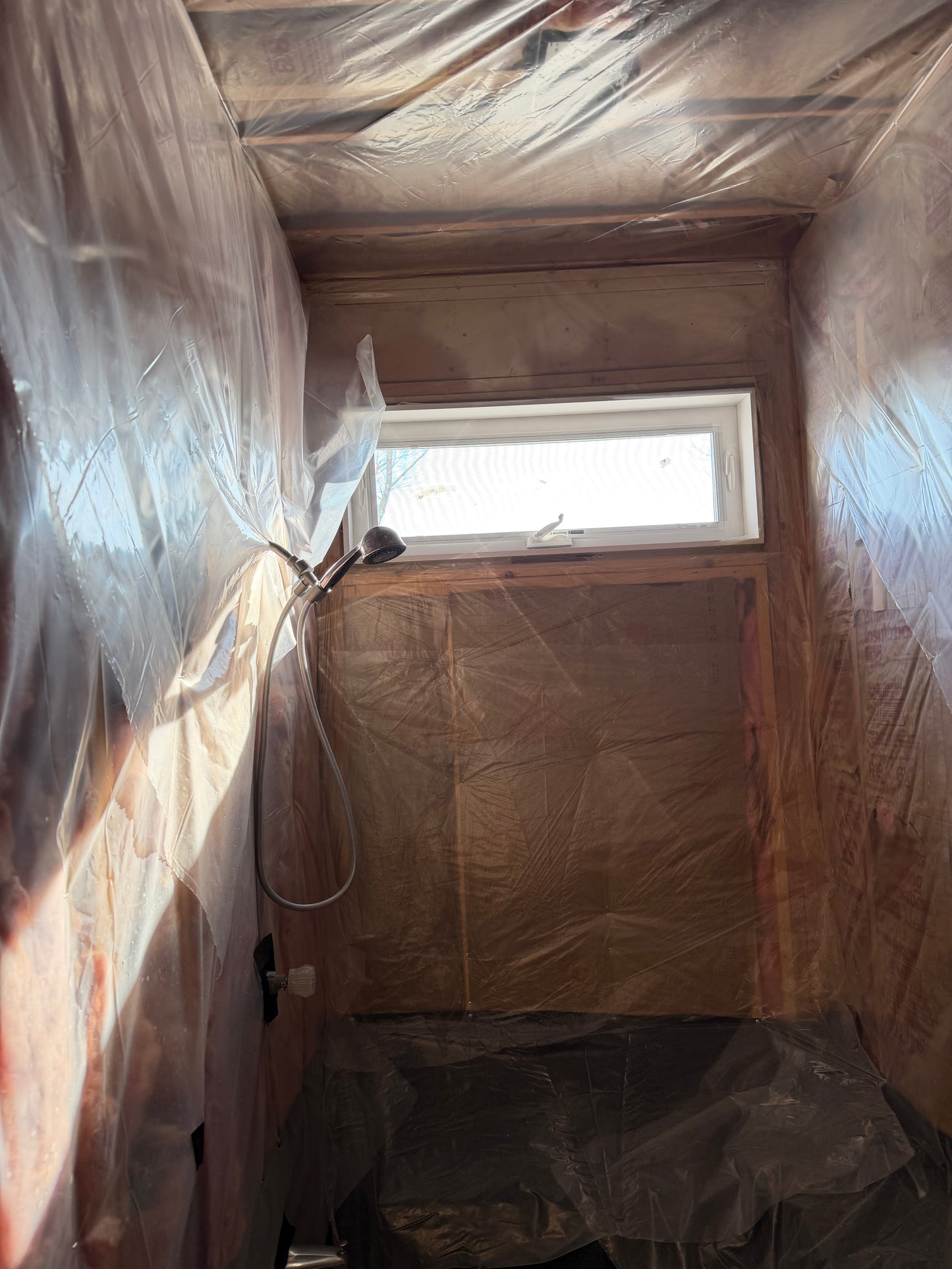 Shower under construction with plastic sheeting on floor and walls