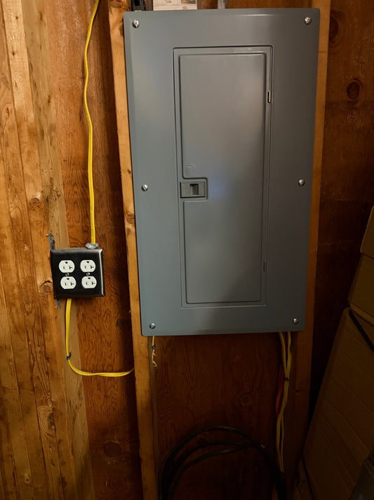 Metal electrical panel on a wooden wall with wiring.