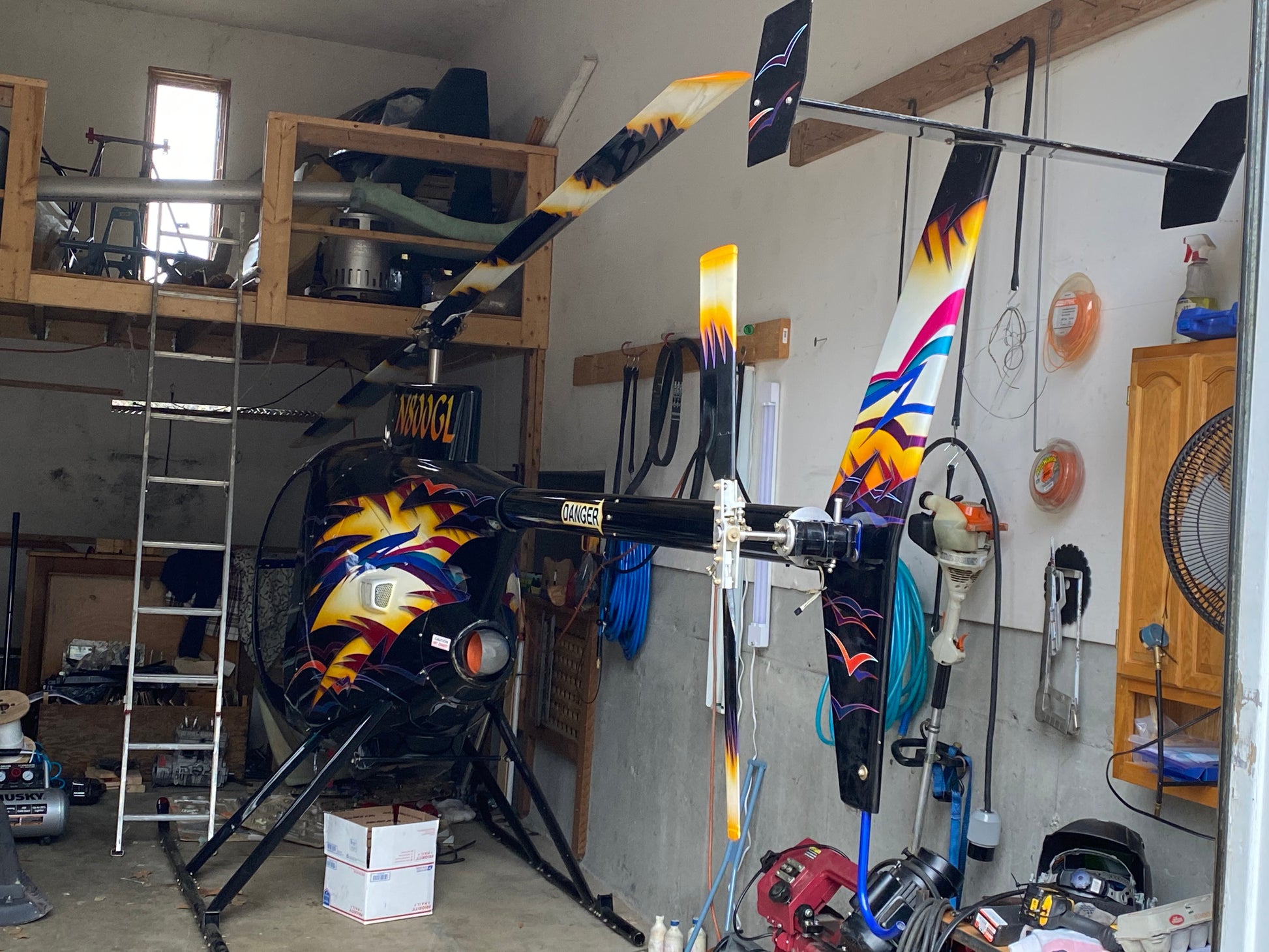Colorful helicopter rotor blades hanging in a workshop with tools and equipment around.
