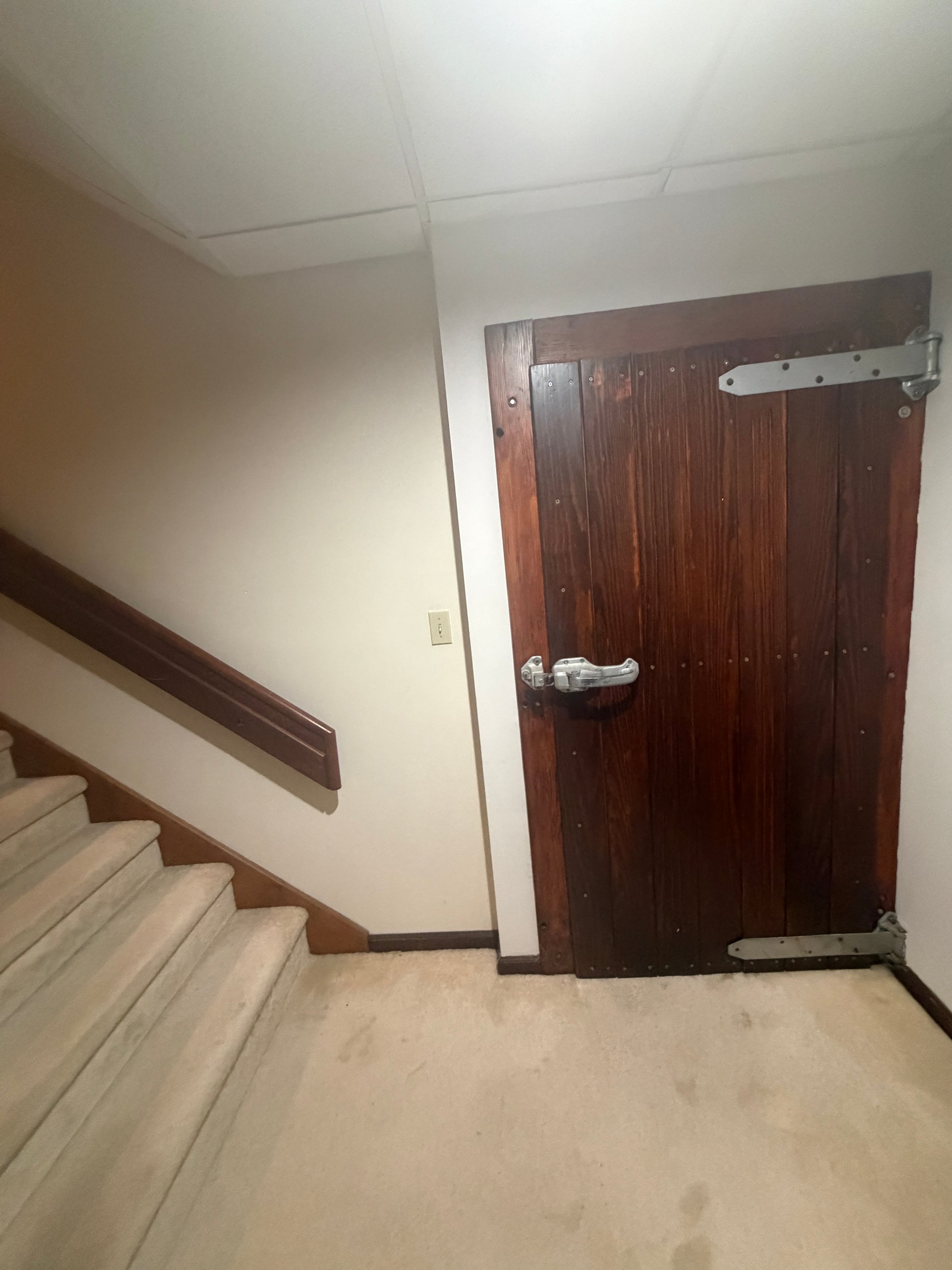Thick wooden door to wine cellar on a wall next to a staircase