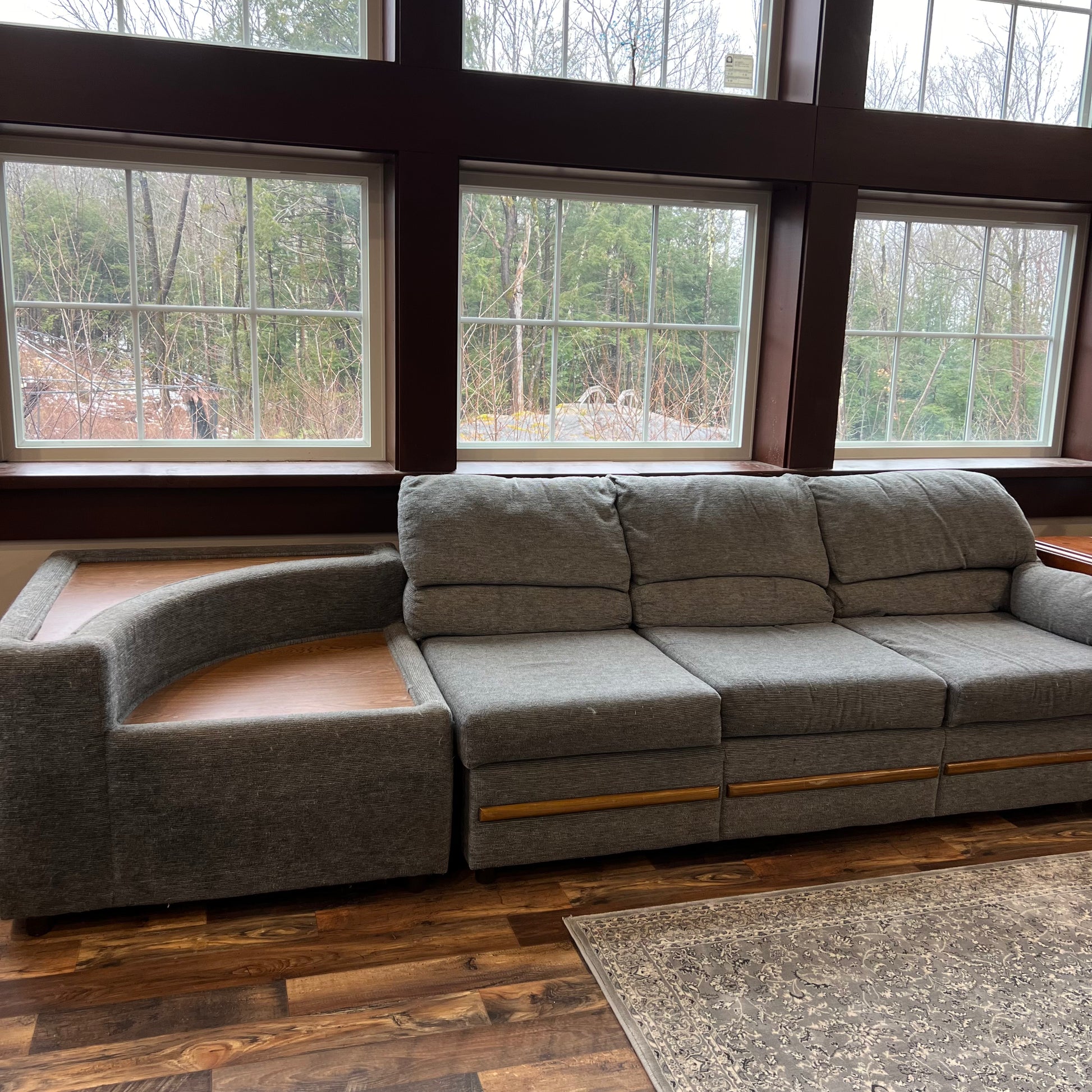 Gray sectional sofa in a room with large windows showing trees outside.