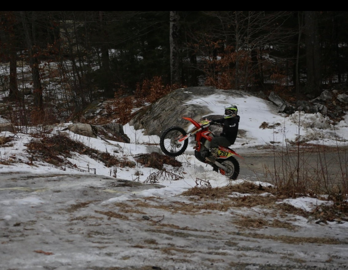Person riding a dirt bike  running the motocross track with studded tires for ice riding on a snowy trail with trees in the background. Nature View Estate