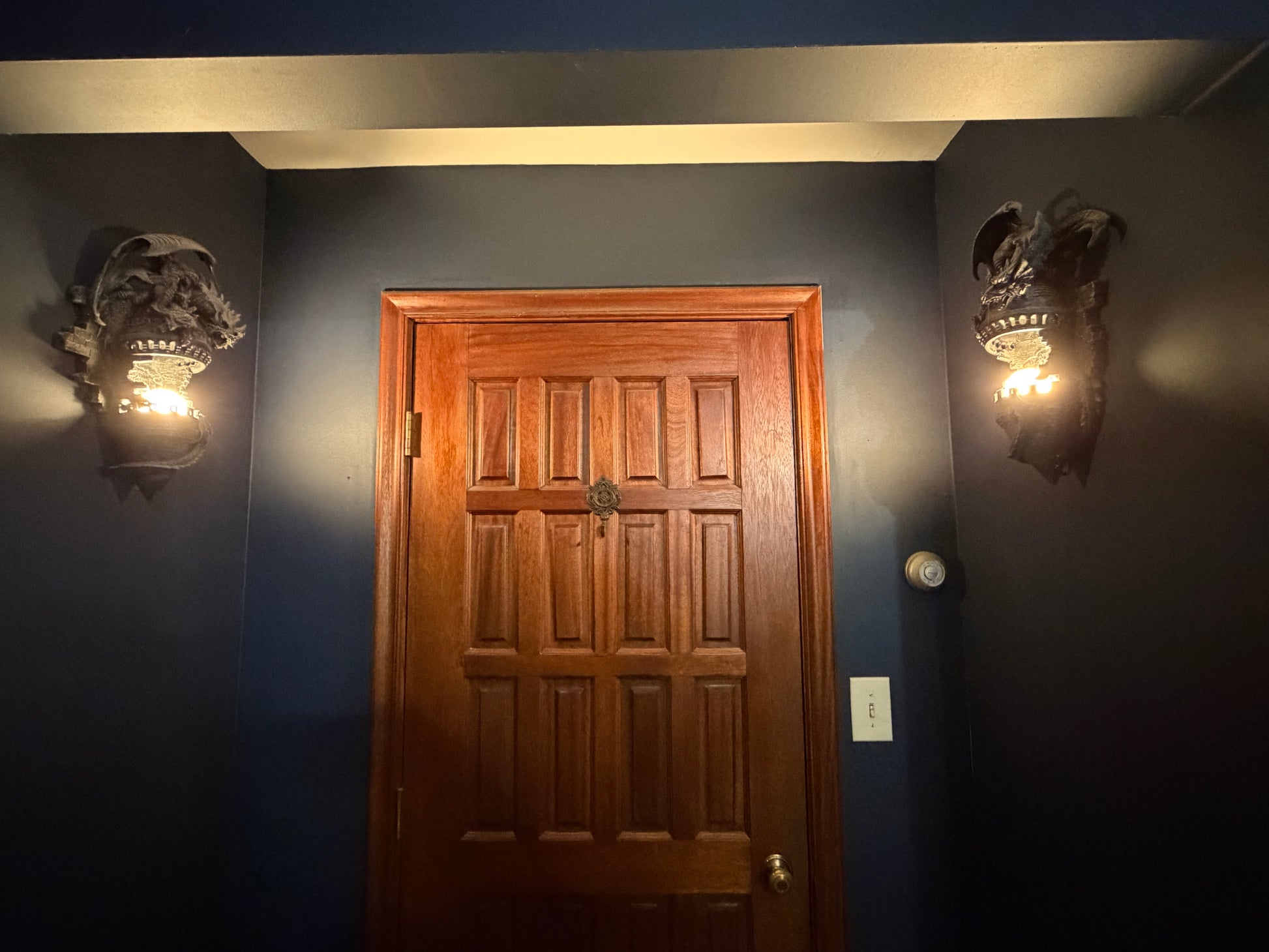 Walk in closet  in the master bedroom 20 panel mahogany door between two dragon wall sconces with lights on a dark blue wall.