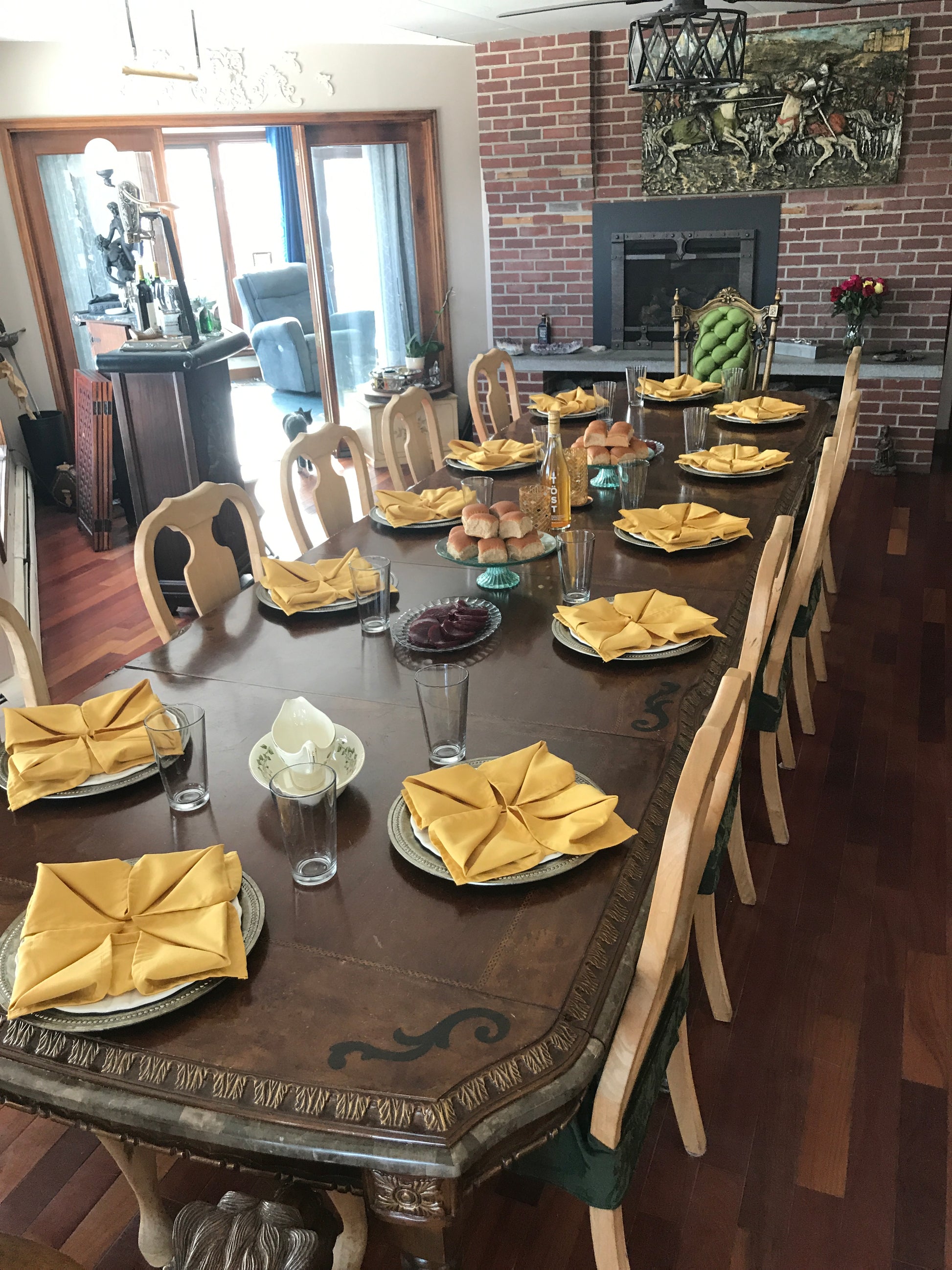 Dining table set with yellow napkins and glassware in a room with a brick wall and large window and fireplace.  Nature View NH Estate