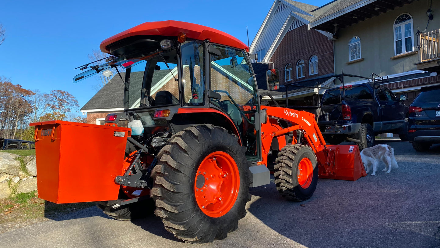 Orange tractor with large wheels in a parking lot with buildings in the background