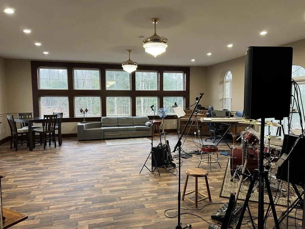 Large music room with wooden flooring, large windows, and musical equipment.