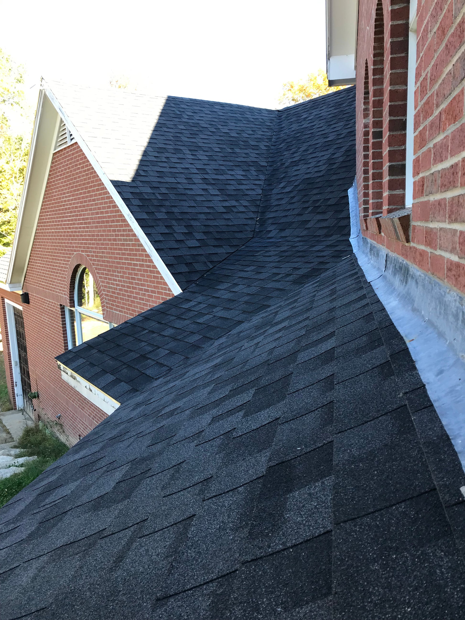 Close-up of a roof with dark shingles and a brick building in the background.