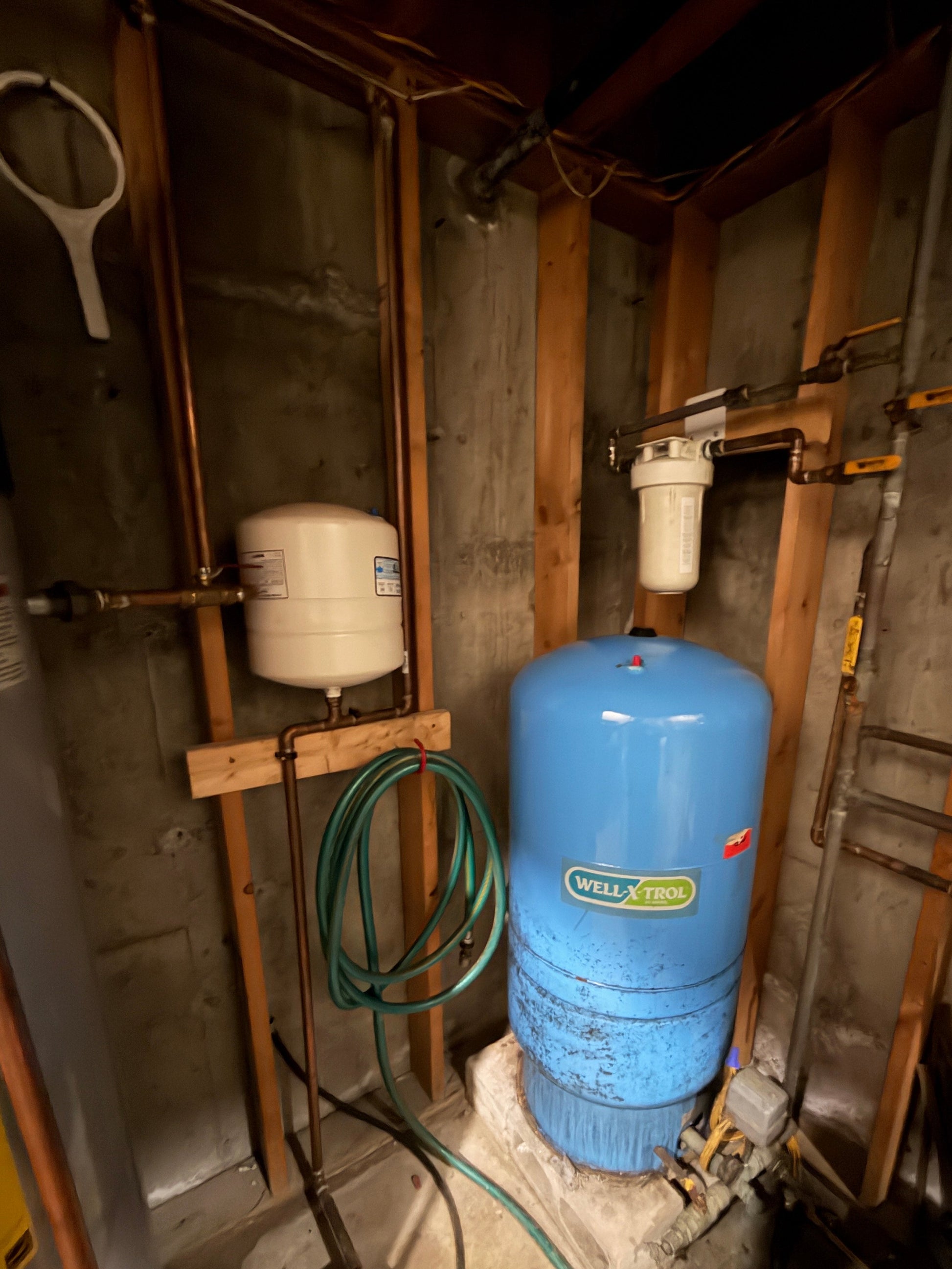 Blue water tank and white pressure tank in a basement setting with pipes and hoses.