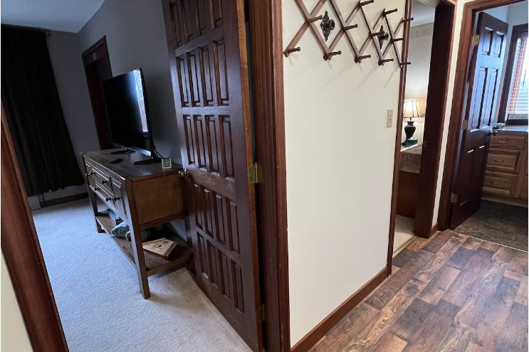 Passageway between two rooms with wooden doors and furniture.