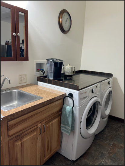 Small kitchenette with washing machine, dryer, sink, and cabinets.