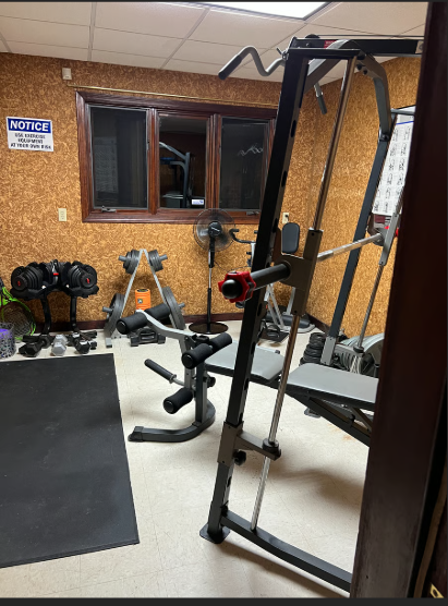 Home gym with weightlifting equipment against a cork wall.