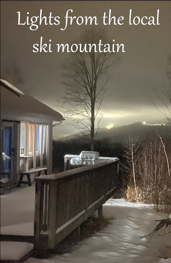 Snowy outdoor scene with  lights from a ski mountain in the background.