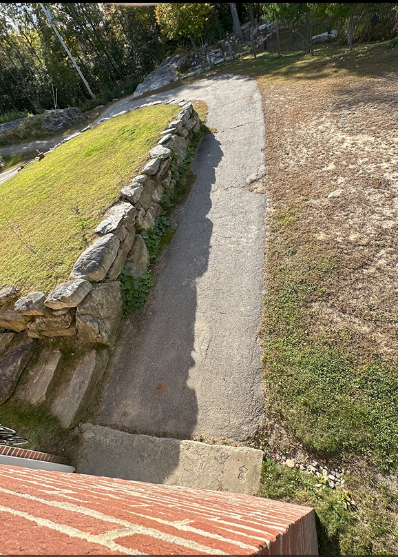 Stone retaining wall with a natural landscape with grass and trees. against brick house