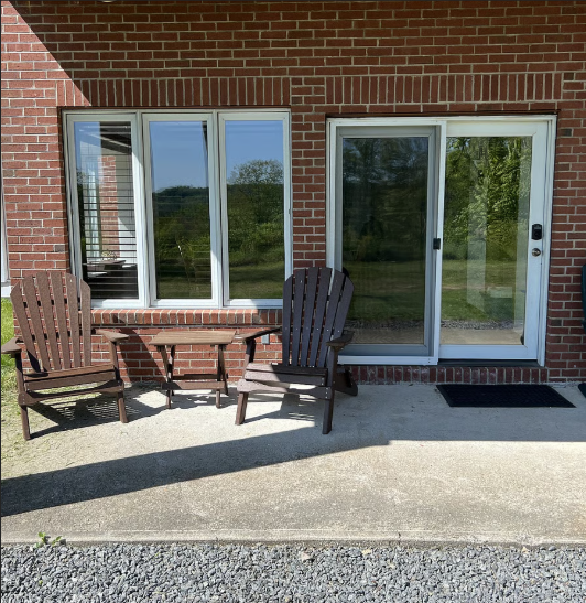 Outdoor patio with wooden chairs and table against a brick wall with sliding glass door.