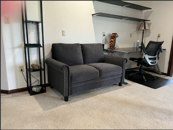 Gray sofa in a room with a desk and shelves.