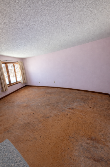 Empty room with textured ceiling and walls, wooden floor, and a window.