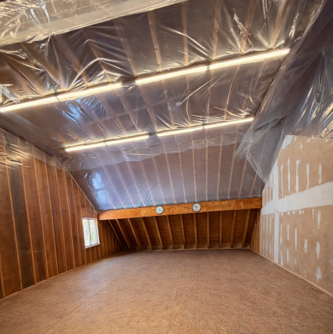 Attic space with plastic wrap on the ceiling and wooden beams.