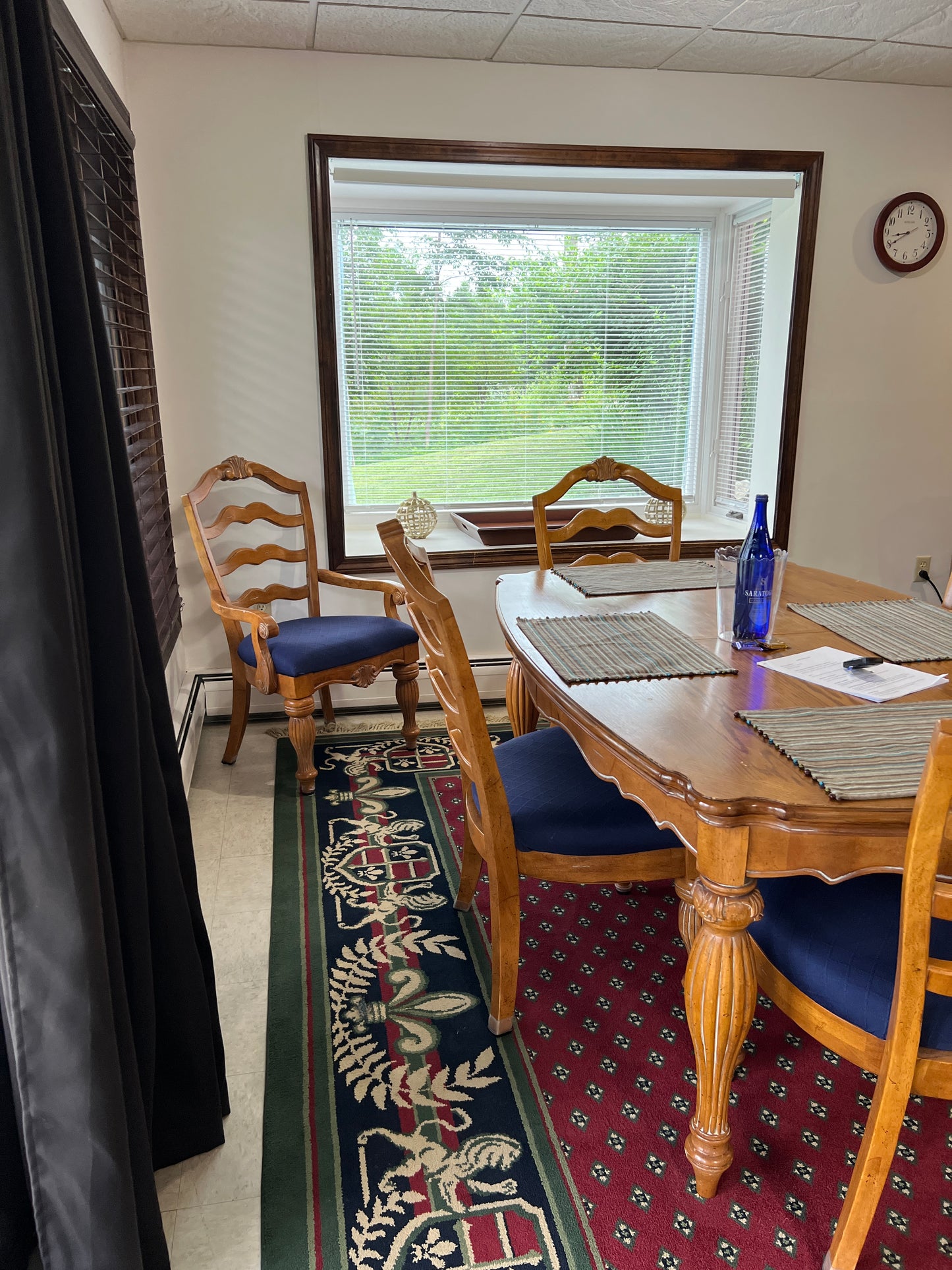 Wooden chair with a blue cushion in front of a window with a decorative rug on the floor.