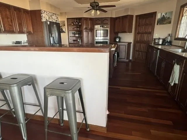 Kitchen with wooden cabinets, stainless steel appliances, and metal stools seating  for 4-5 at the bar. in between dining room and kitchen