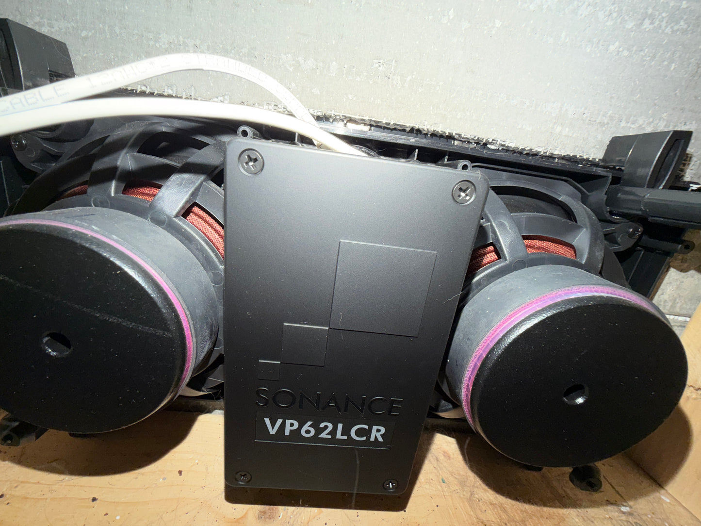 Close-up of a Sonance speaker system with two subwoofers on a wooden surface.