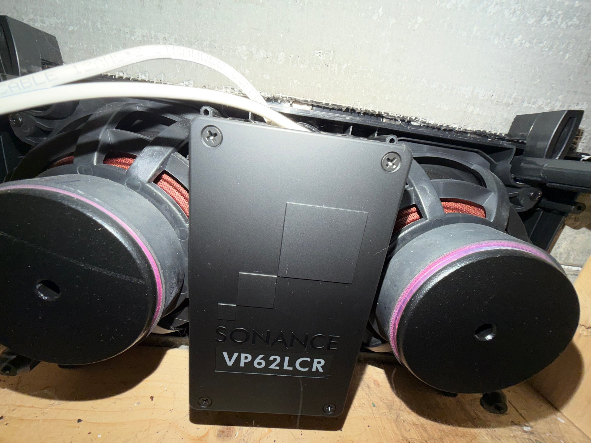 Close-up of a Sonance speaker system with two subwoofers on a wooden surface.